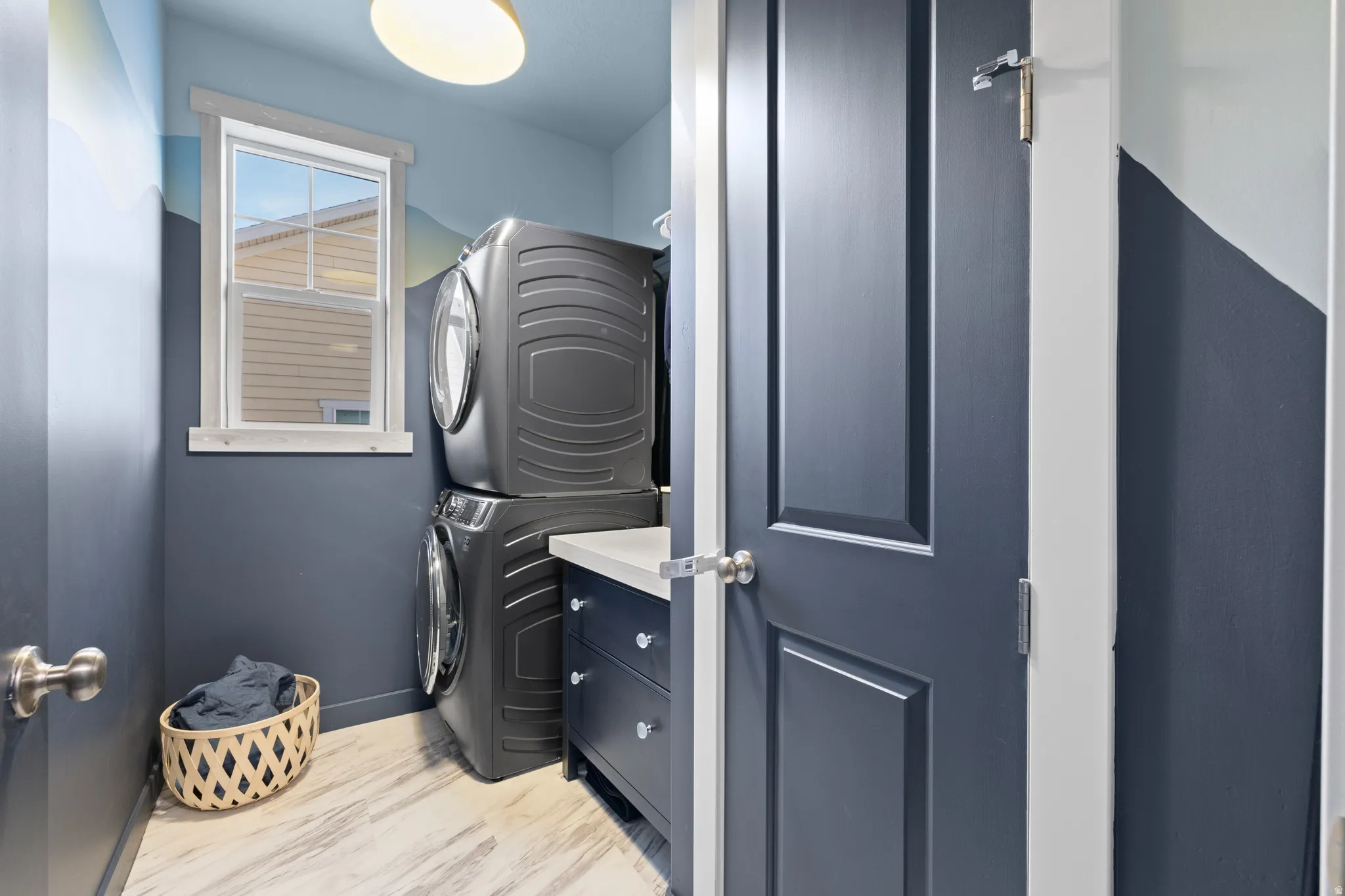 Laundry area with stacked washing machine and dryer and light wood-style flooring