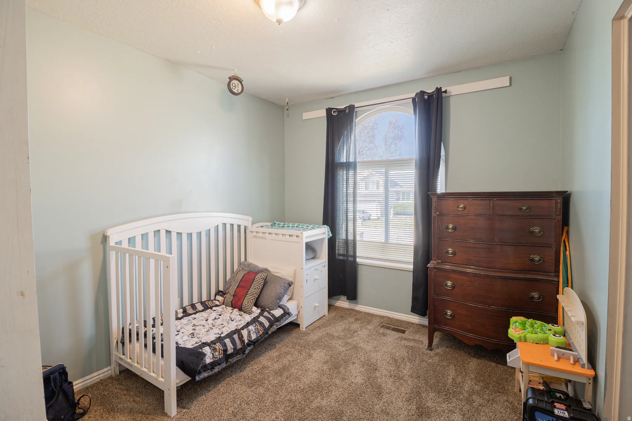 Bedroom with a nursery area, dark colored carpet, and a textured ceiling