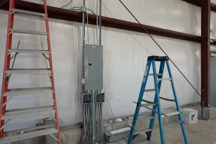 Miscellaneous room featuring unfinished concrete flooring, electric panel, and metal wall