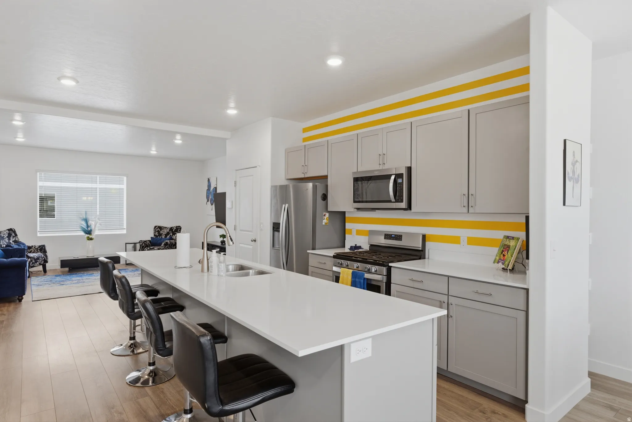 Kitchen with a breakfast bar area, stainless steel appliances, light wood-style floors, an island with sink, and gray cabinetry