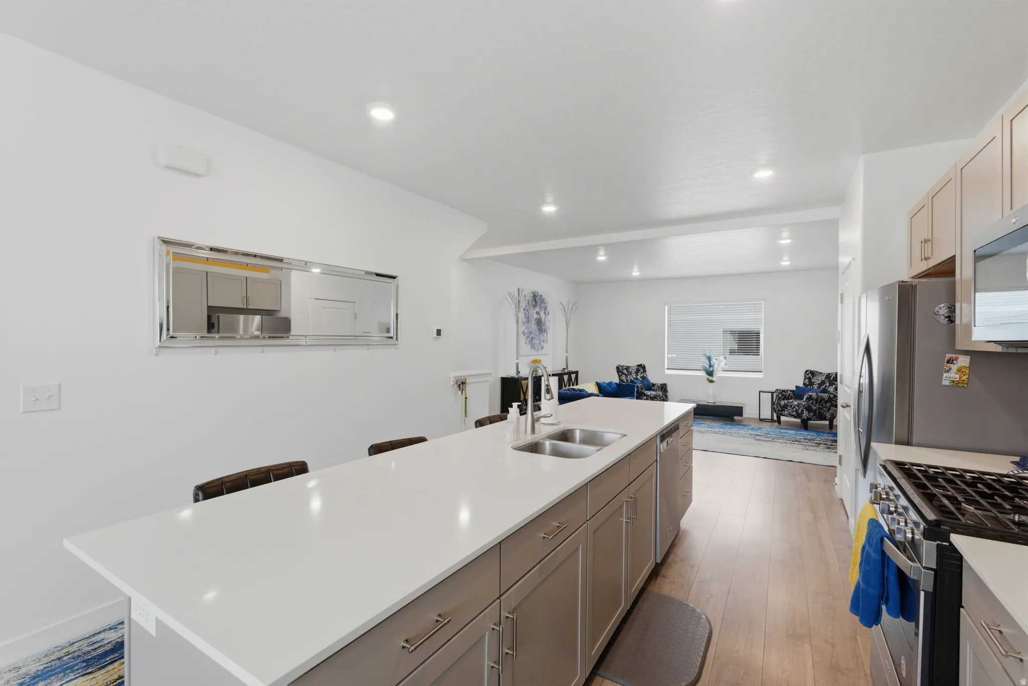 Kitchen featuring a kitchen island with sink, light wood-style flooring, stainless steel appliances, a breakfast bar area, and light stone countertops