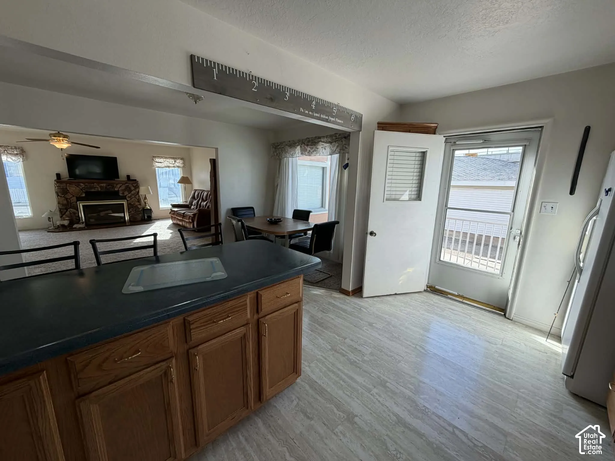 Kitchen with freestanding refrigerator, dark countertops, ceiling fan, a fireplace, and wood finish cabinets