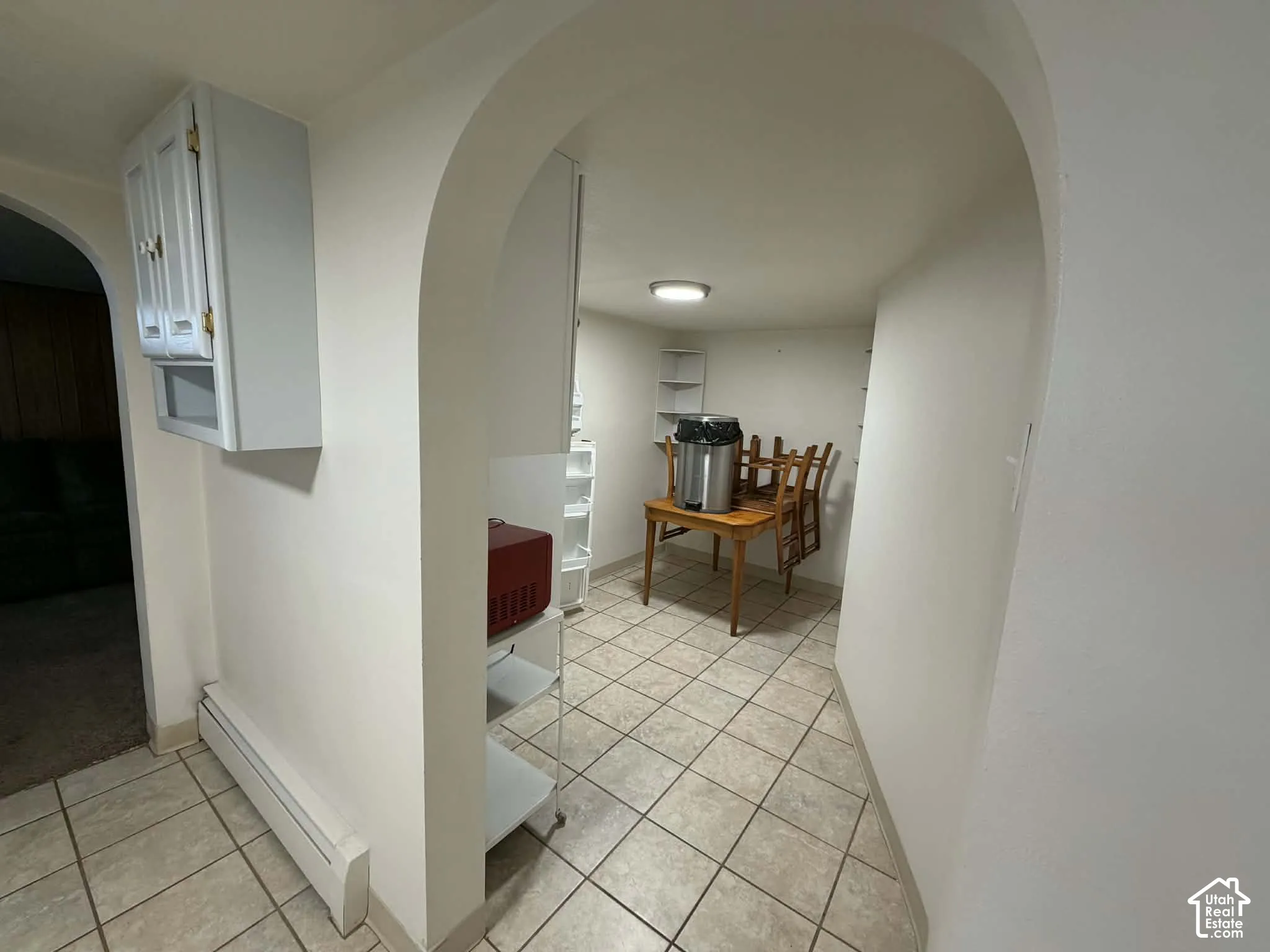 Corridor featuring arched walkways, baseboard heating, and light tile patterned floors