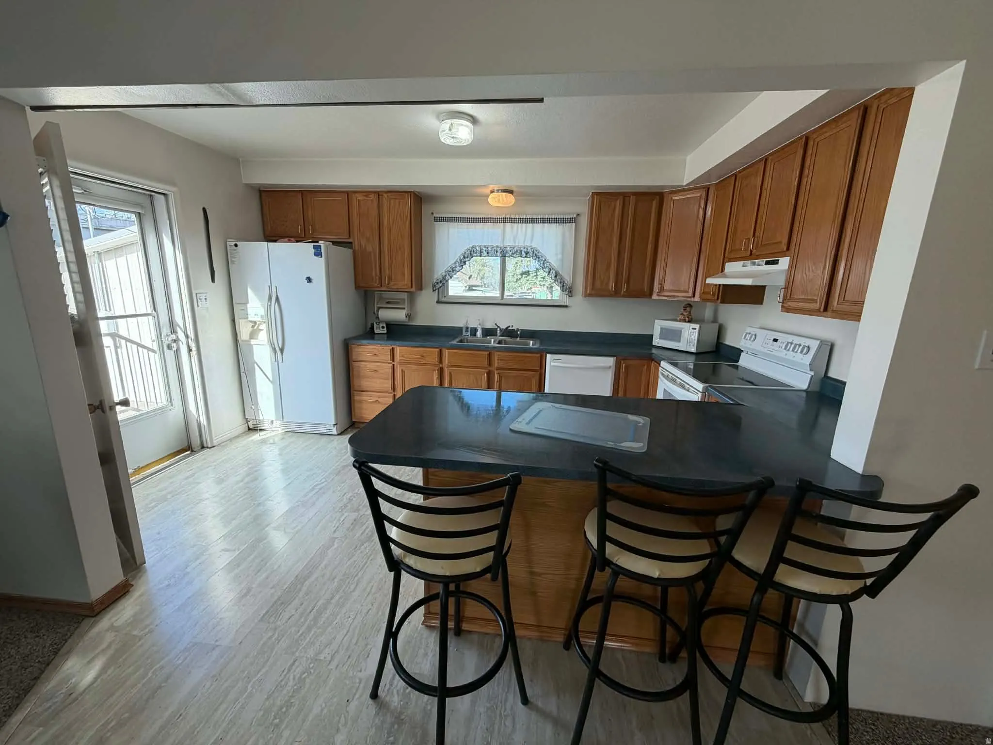 Kitchen featuring wood finish cabinetry, a breakfast bar, white appliances, and a peninsula