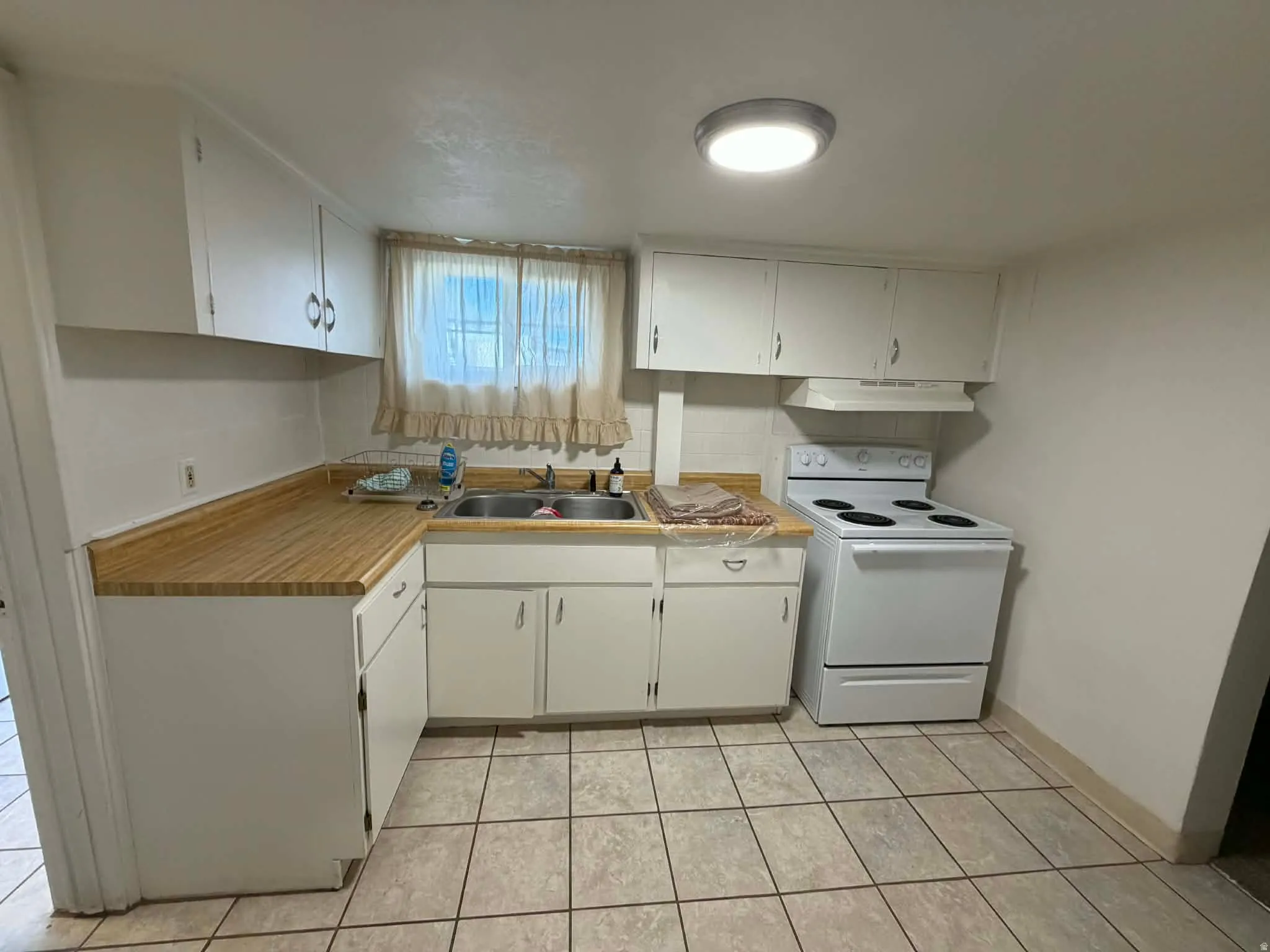 Kitchen with white electric stove, white cabinetry, light countertops, and light tile patterned floors