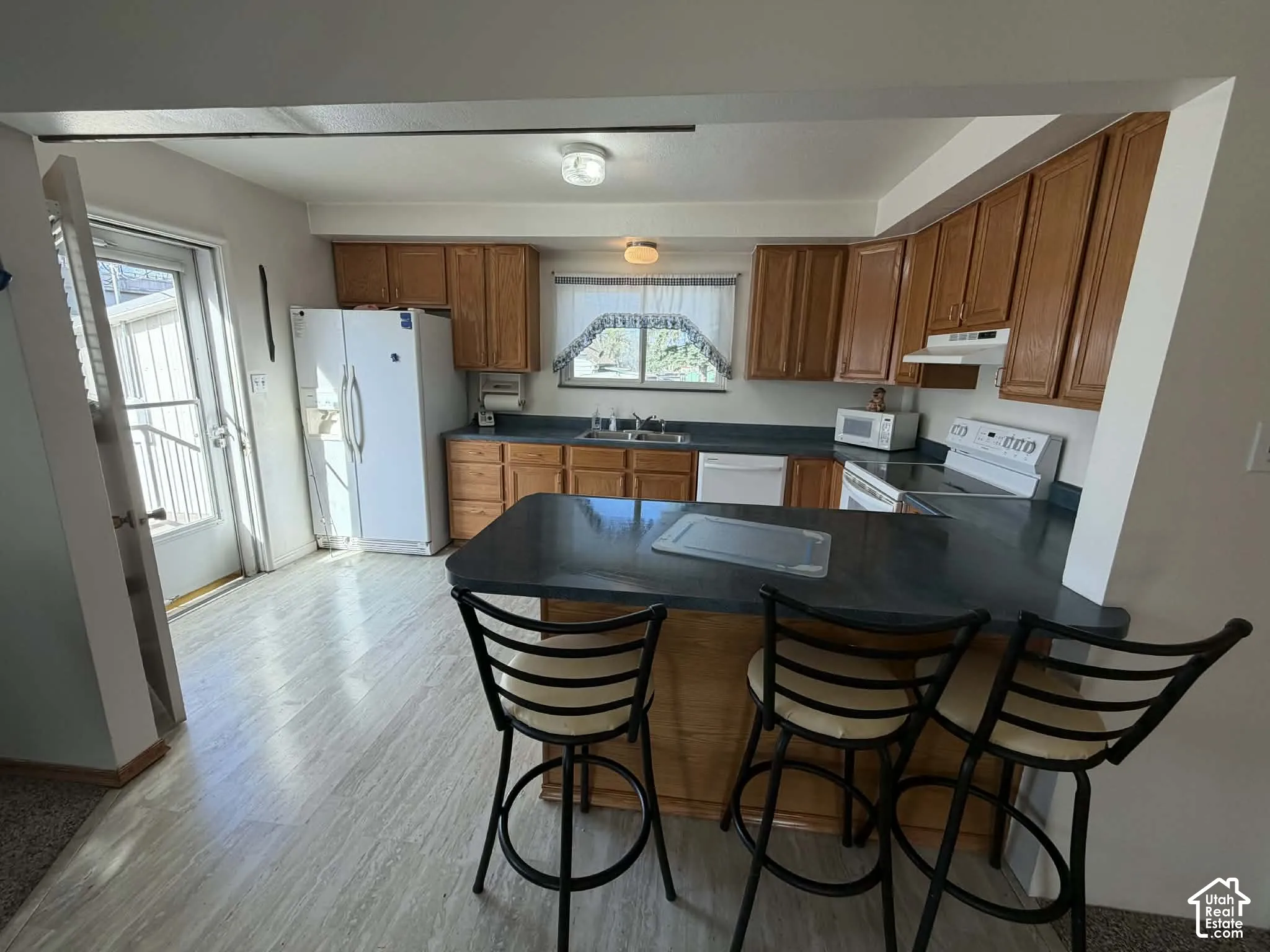 Kitchen featuring wood finish cabinetry, a breakfast bar, white appliances, and a peninsula