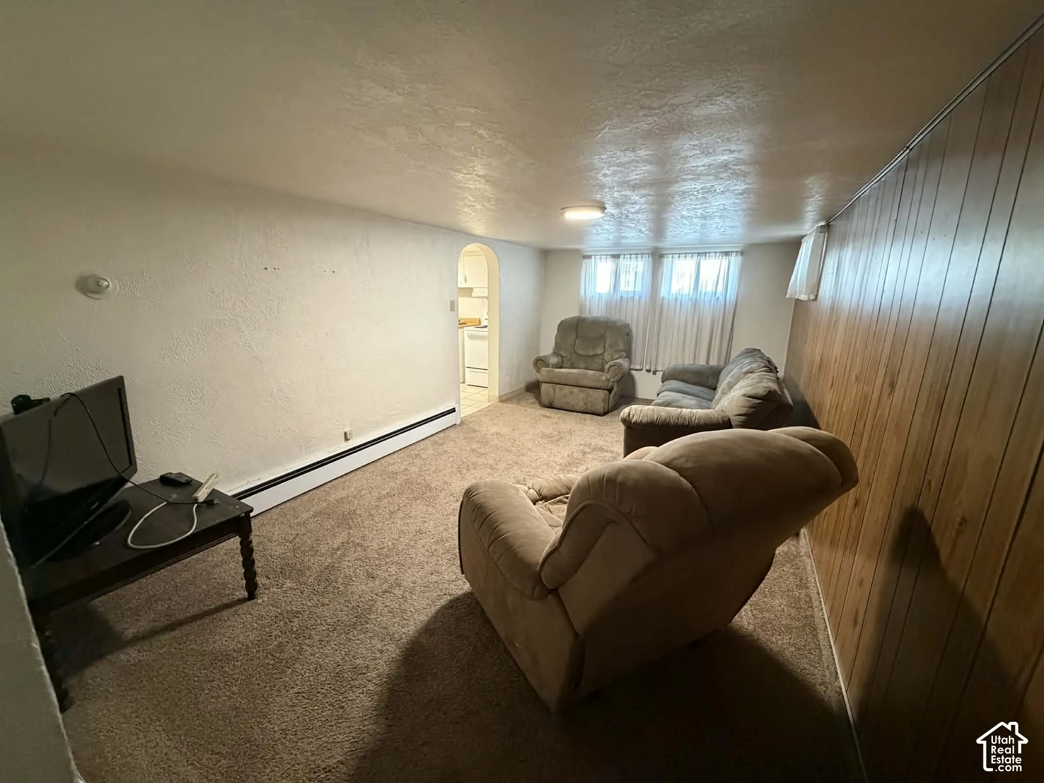 Carpeted living area featuring a textured ceiling, a baseboard radiator, arched walkways, and a textured wall
