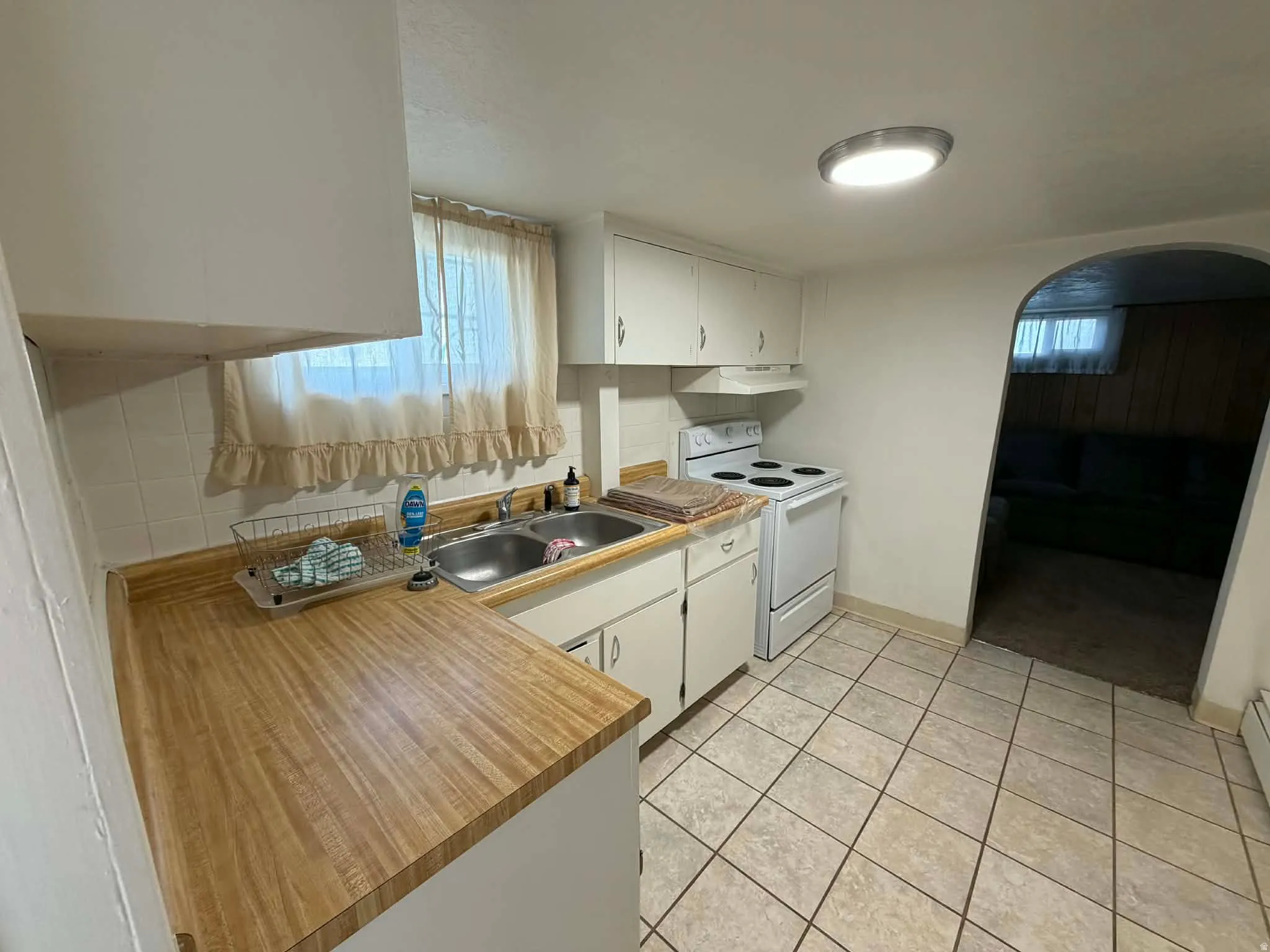 Kitchen with white cabinets, white range with electric cooktop, tasteful backsplash, and light countertops