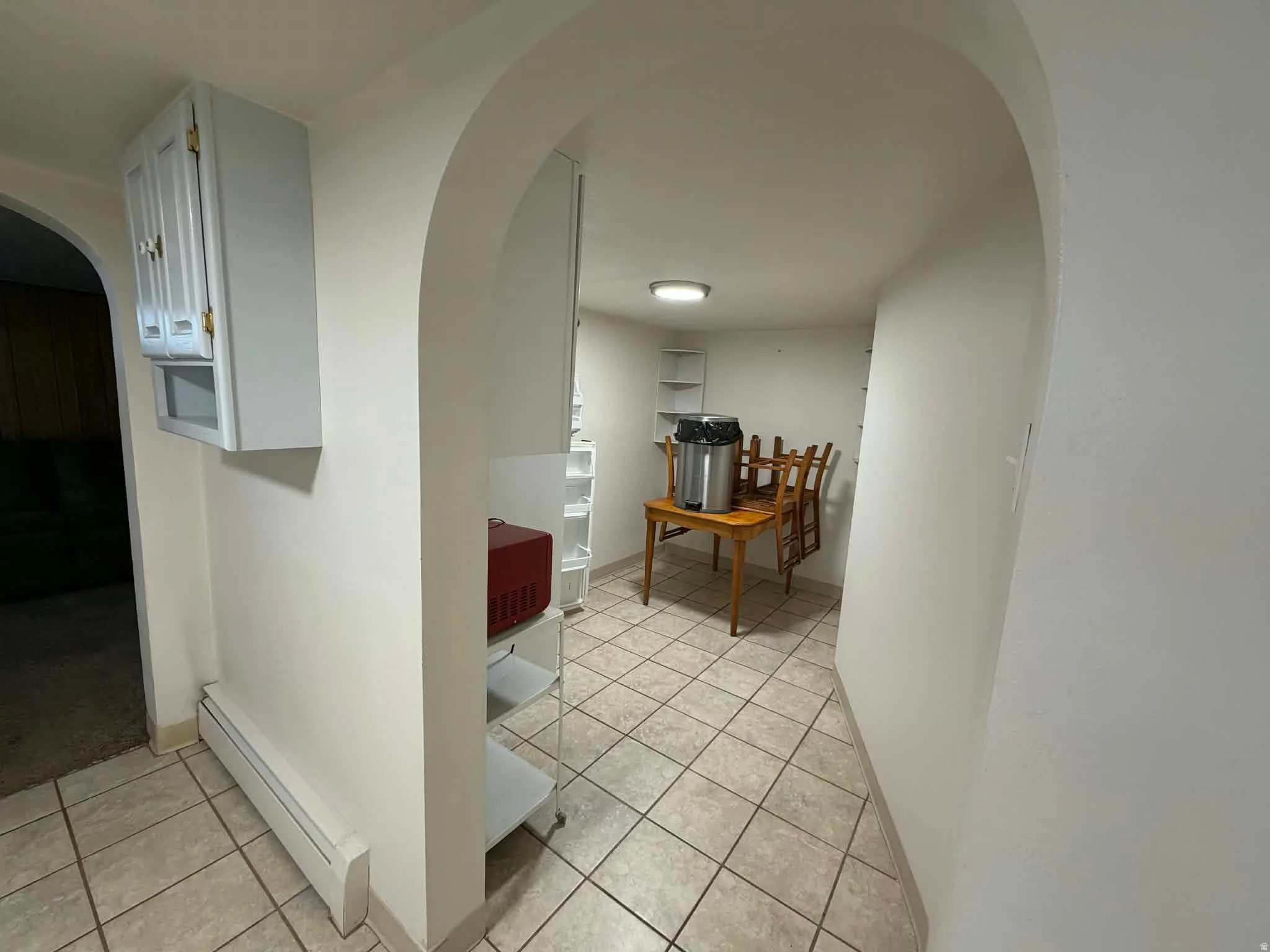 Corridor featuring arched walkways, baseboard heating, and light tile patterned floors