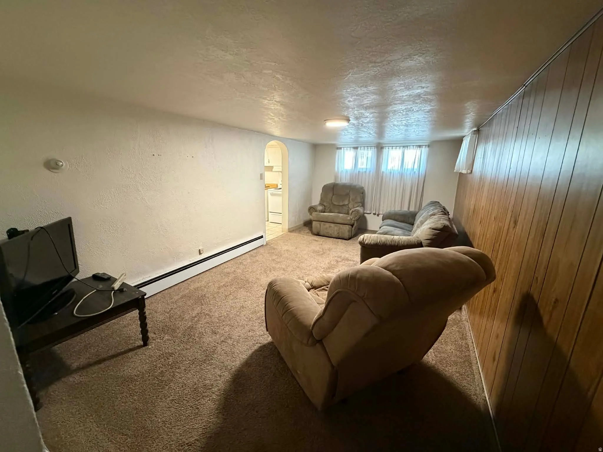 Carpeted living area featuring a textured ceiling, a baseboard radiator, arched walkways, and a textured wall