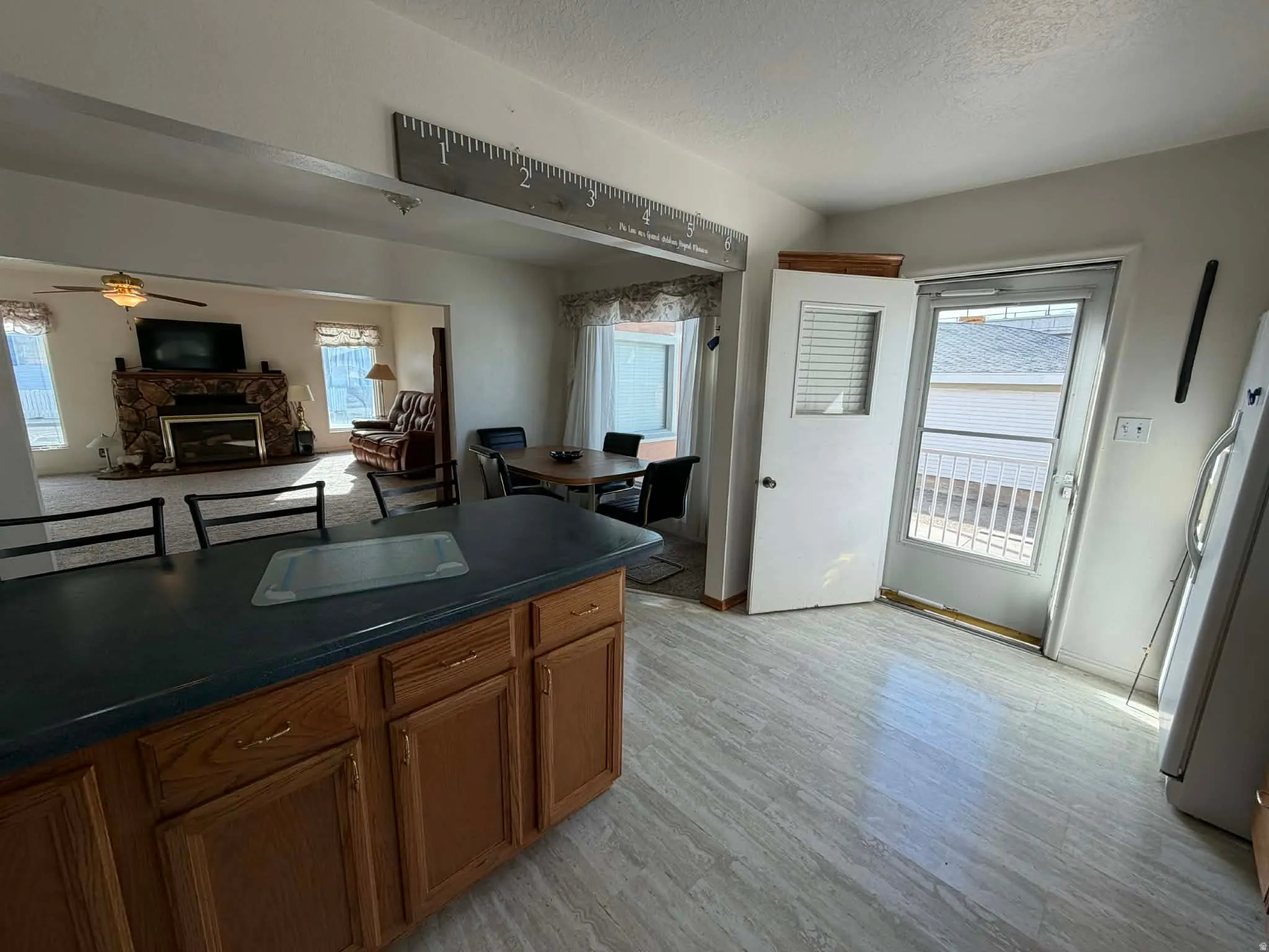Kitchen with freestanding refrigerator, dark countertops, ceiling fan, a fireplace, and wood finish cabinets