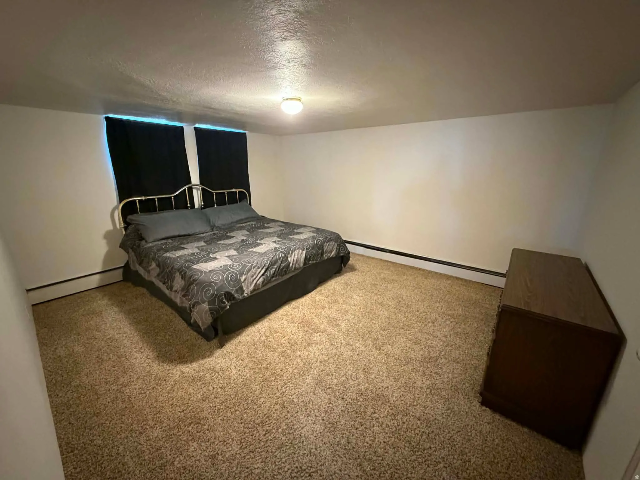 Carpeted bedroom featuring a baseboard heating unit and a textured ceiling