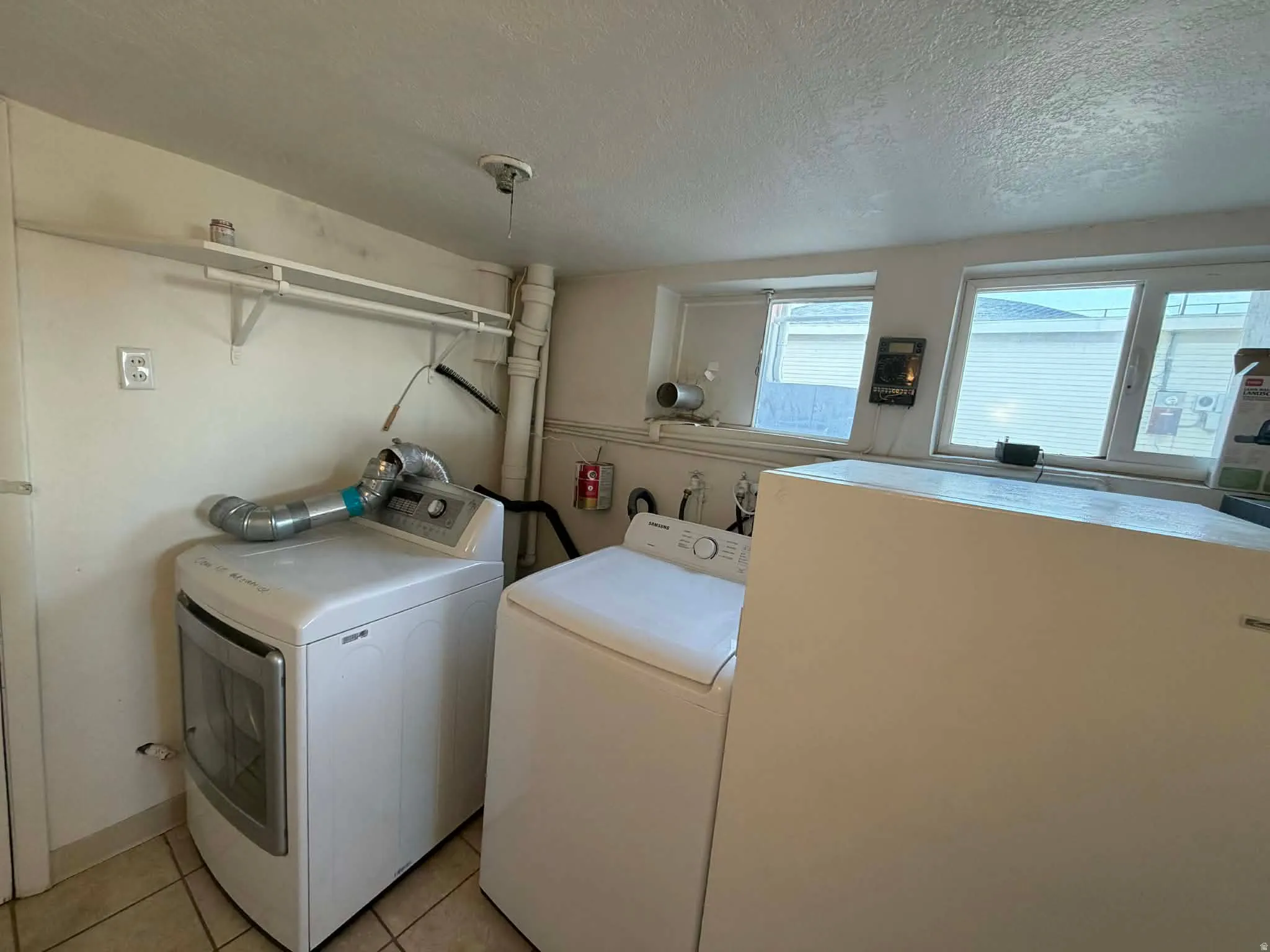 Laundry room with a textured ceiling, washer and clothes dryer, and light tile patterned flooring
