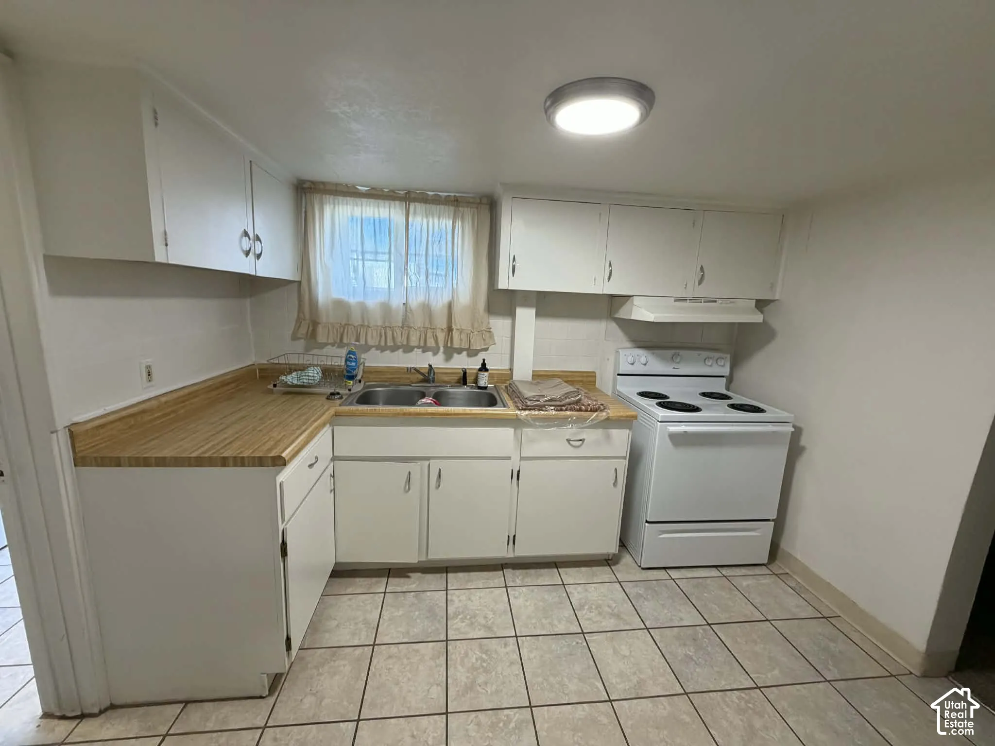 Kitchen with white electric stove, white cabinetry, light countertops, and light tile patterned floors