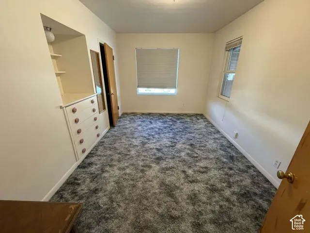 Unfurnished bedroom with dark colored carpet and baseboards