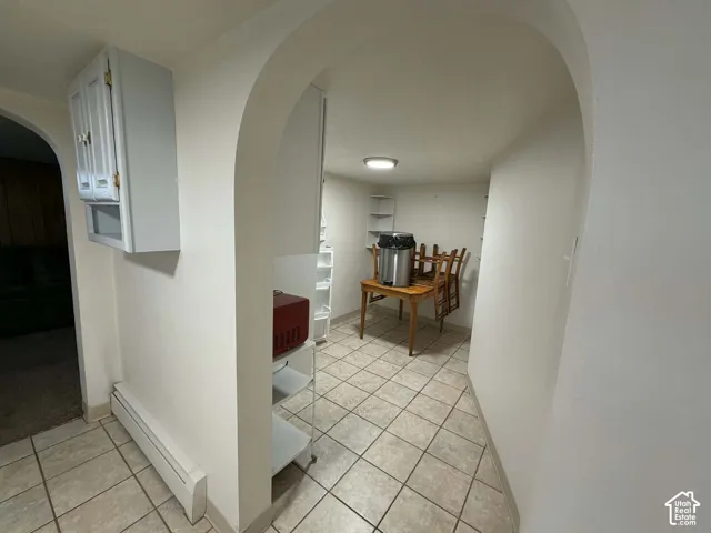 Corridor featuring arched walkways, baseboard heating, and light tile patterned floors
