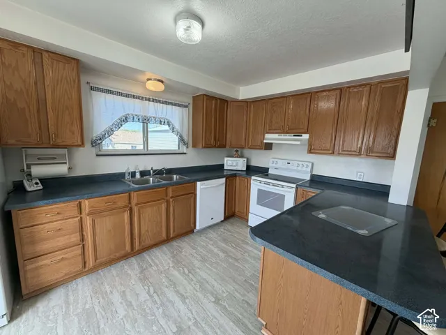 Kitchen featuring dark countertops, wood finish cabinets, white appliances, a textured ceiling, and light wood-style floors
