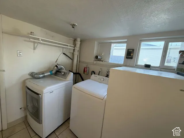 Laundry room with a textured ceiling, washer and clothes dryer, and light tile patterned flooring