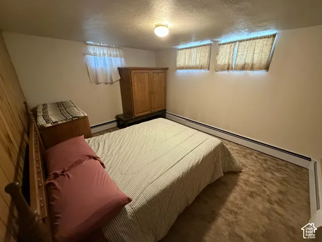 Carpeted bedroom featuring a baseboard heating unit and a textured ceiling