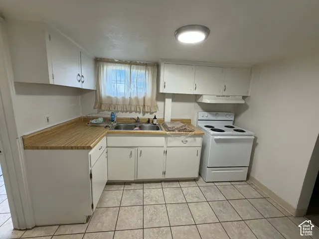 Kitchen with white electric stove, white cabinetry, light countertops, and light tile patterned floors
