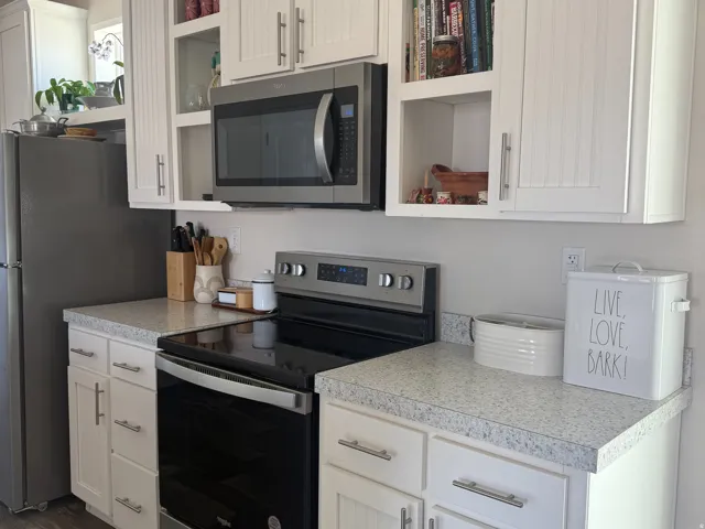 Kitchen featuring stainless steel appliances, light countertops, white cabinets, and dark wood finished floors