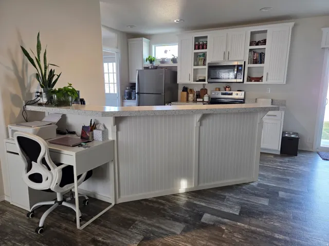 Kitchen with white cabinets, light countertops, stainless steel appliances, dark wood-style flooring, and a breakfast bar area