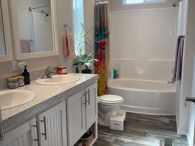 Primary bathroom Full bath featuring double vanity, dark wood-type flooring, and shower / bath combo with shower curtain