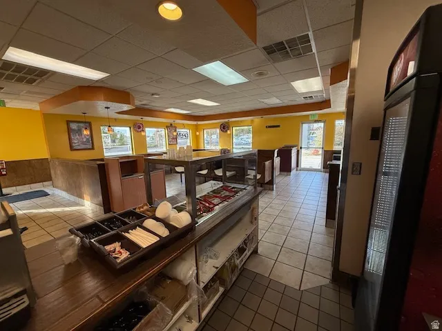 Interior space with a wainscoted wall, light tile patterned flooring, a drop ceiling, and a heating unit