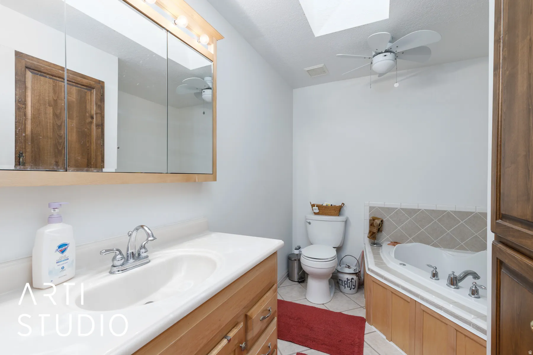 Bathroom featuring a skylight, a ceiling fan, vanity, light tile patterned floors, and a bath
