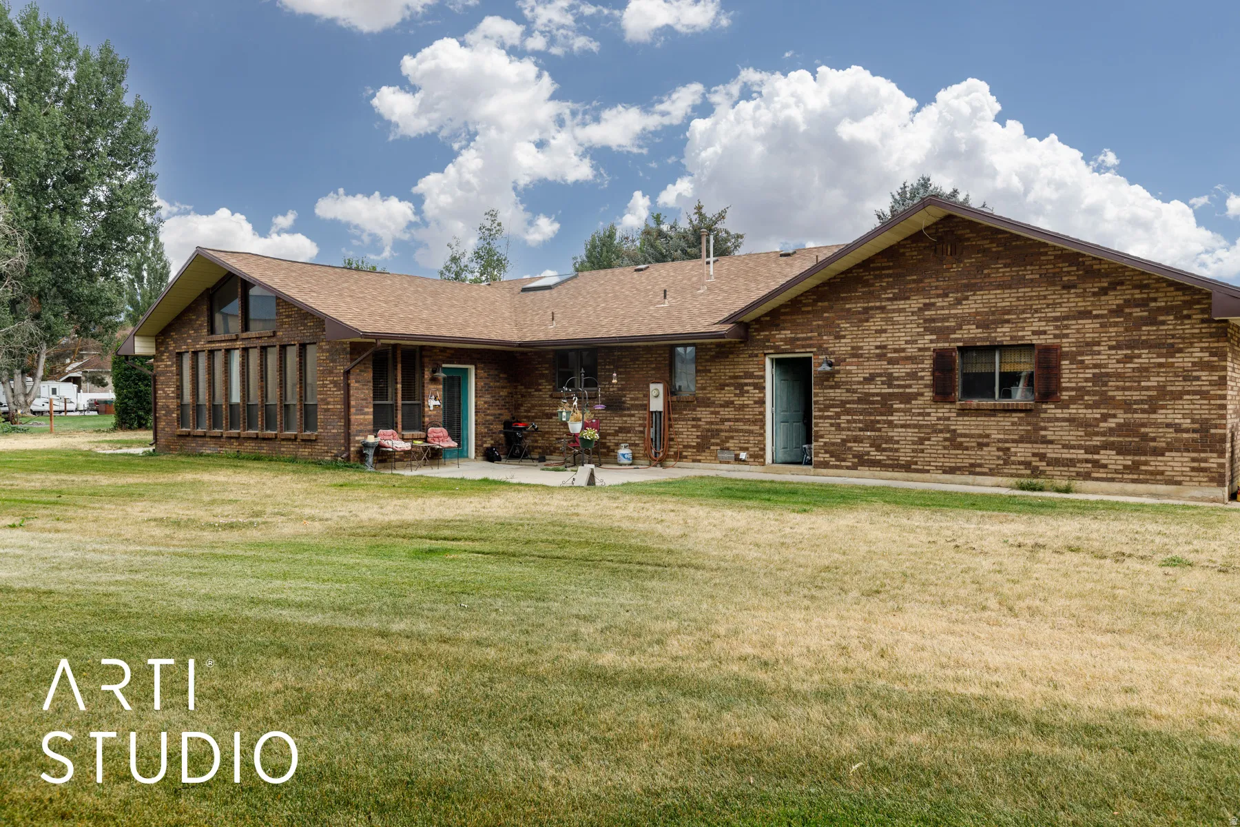 View of back of house with brick siding, a front lawn, a shingled roof, and a patio area