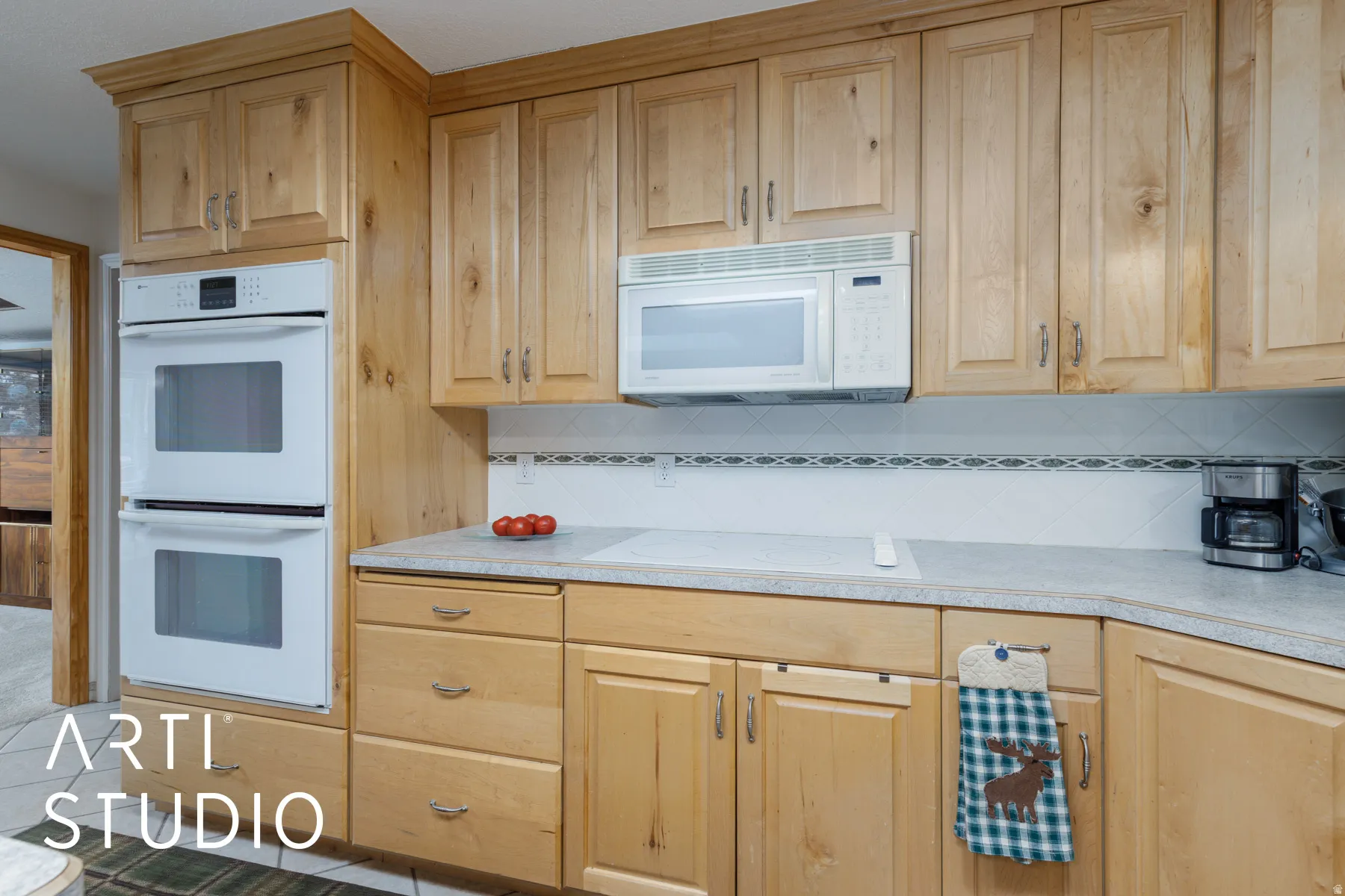 Kitchen featuring white appliances, light countertops, backsplash, and light wood finish cabinets