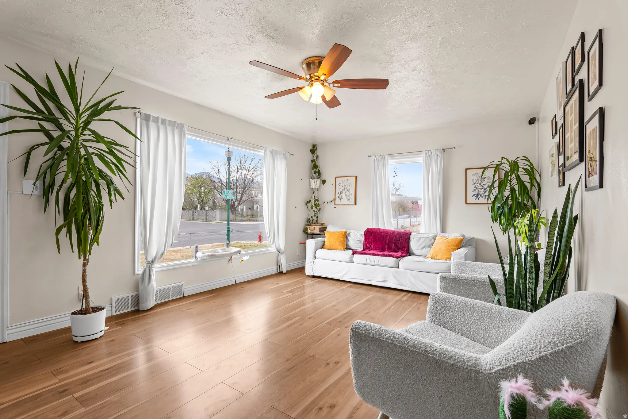 Living area with healthy amount of natural light, light wood-type flooring, a textured ceiling, and ceiling fan