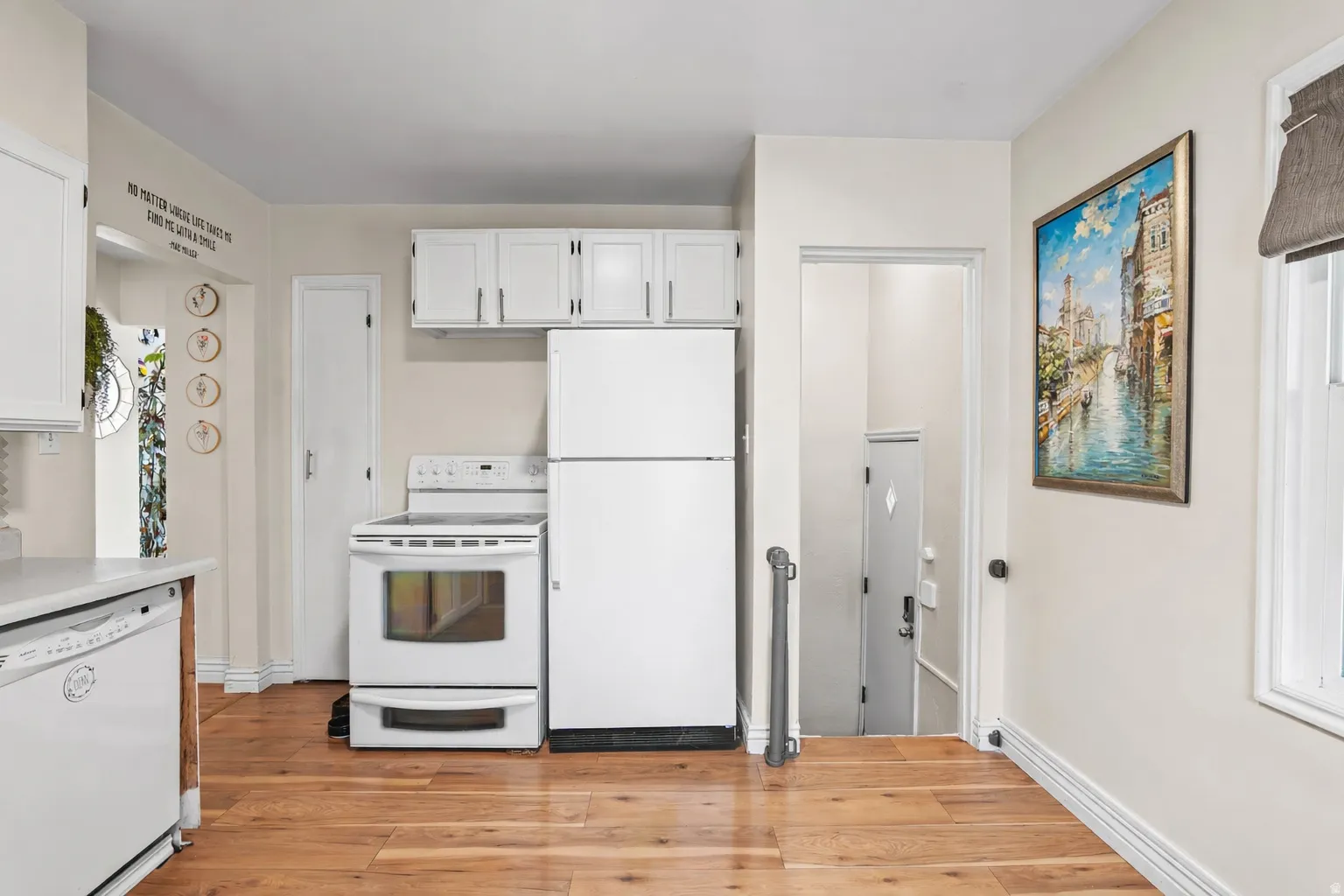 Kitchen with white appliances, white cabinets, light wood-style flooring, and light countertops