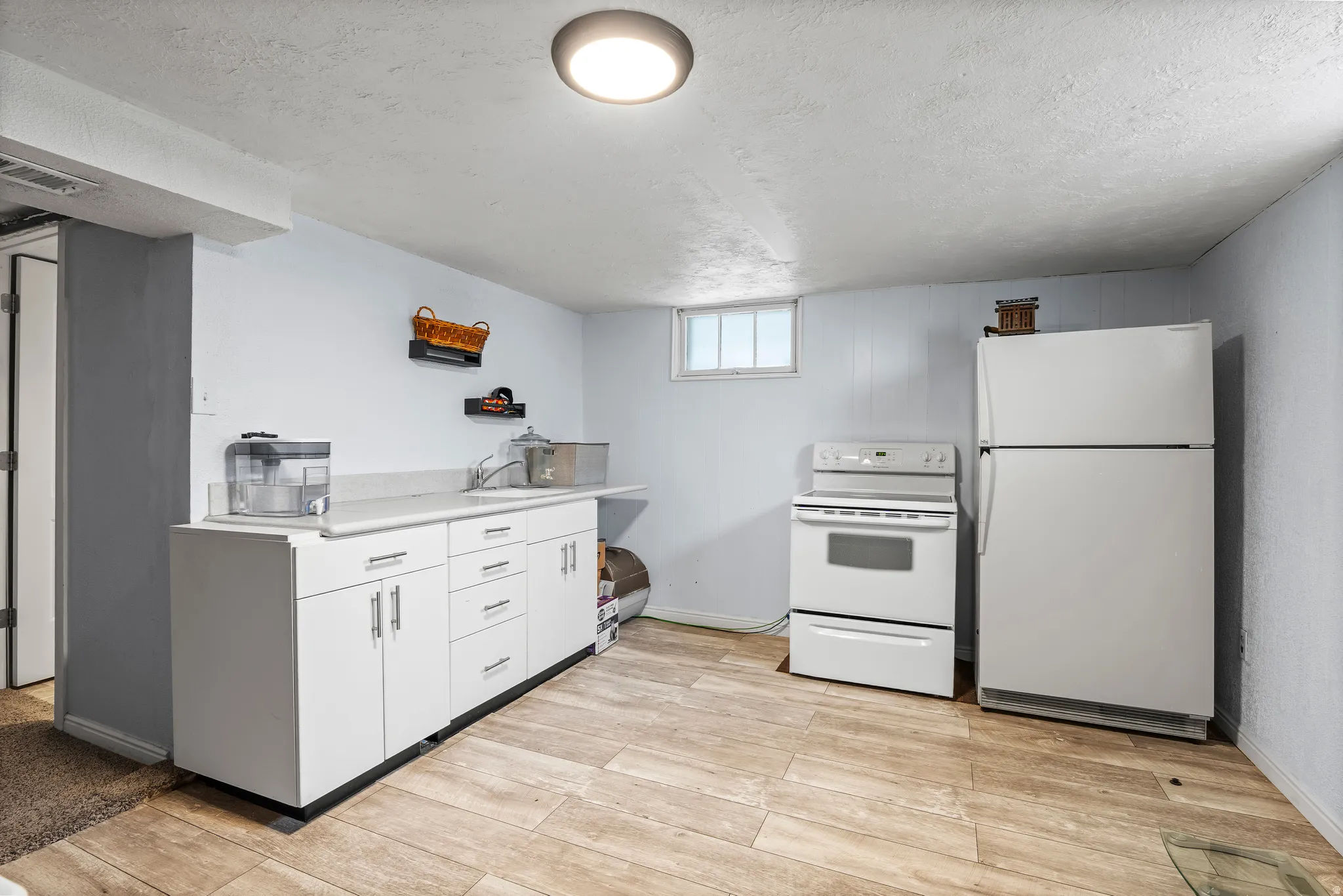 Kitchen with white appliances, light countertops, white cabinetry, a textured ceiling, and light wood finished floors
