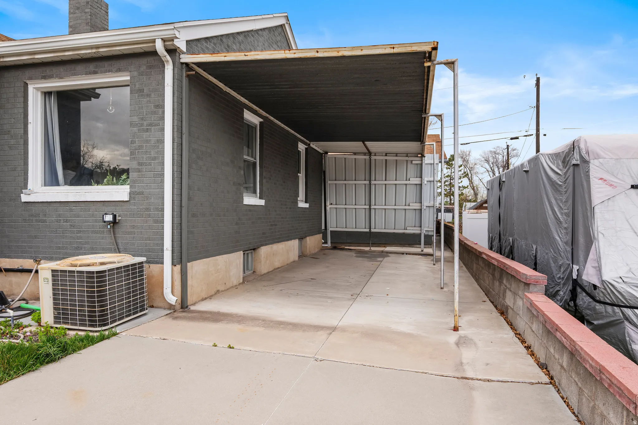 View of home's exterior featuring brick siding, a patio, a chimney, a carport, and concrete driveway