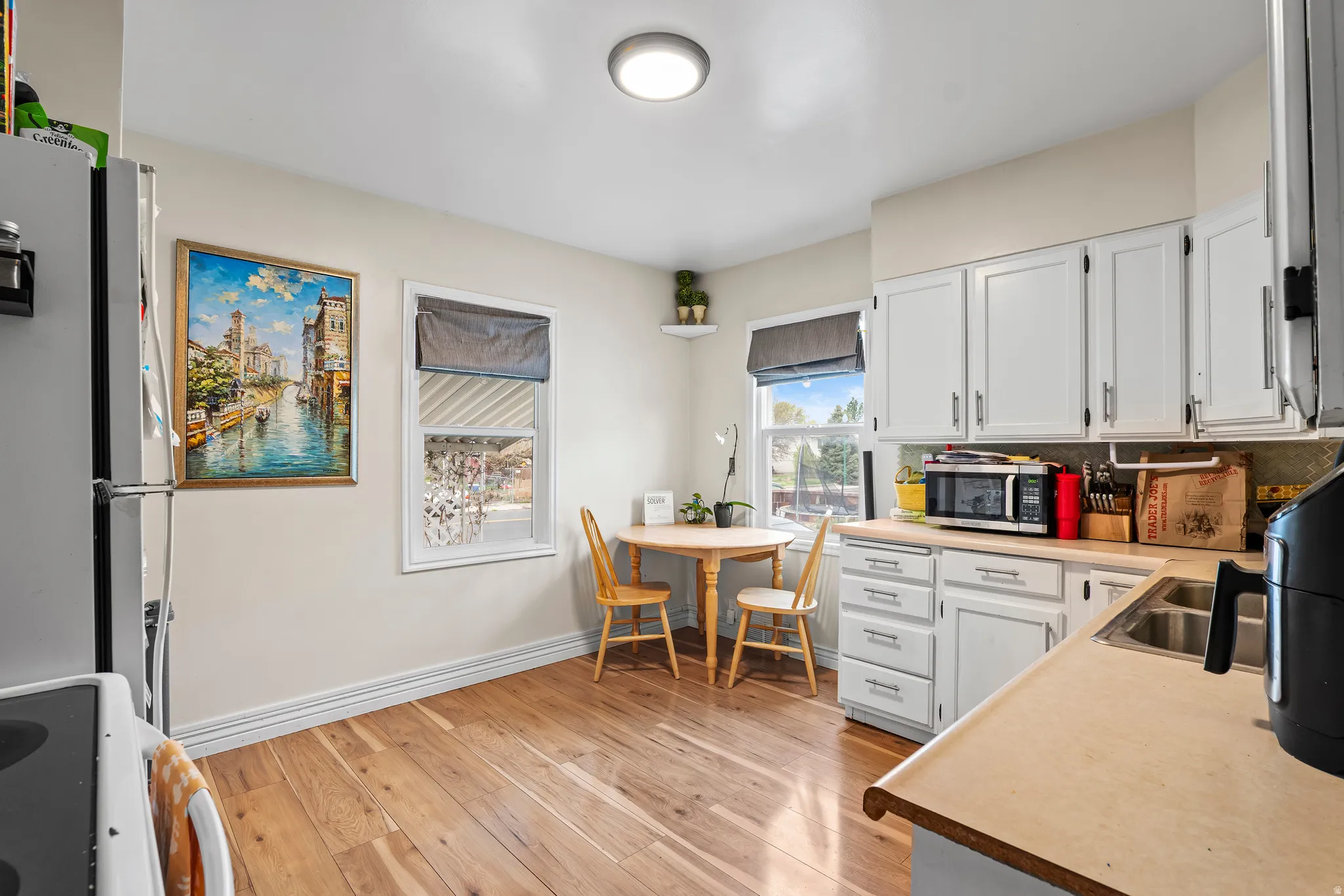 Kitchen featuring stainless steel appliances, light countertops, white cabinets, light wood-type flooring, and backsplash
