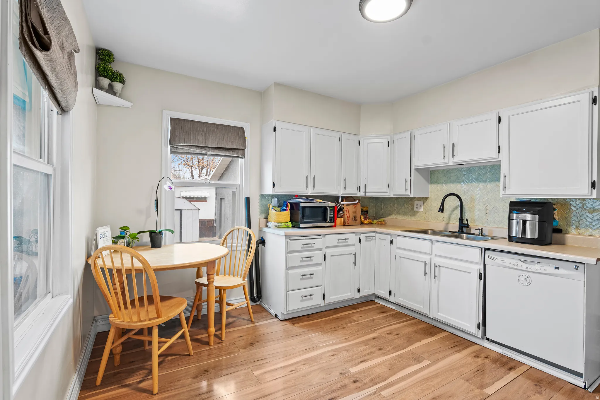 Kitchen with light countertops, light wood-style floors, white dishwasher, and white cabinetry
