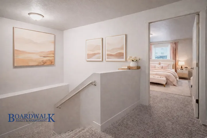 Corridor with an upstairs landing, light colored carpet, and a textured ceiling