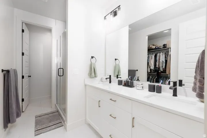 Bathroom with double vanity, a spacious closet, and a stall shower