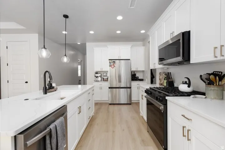 Kitchen with stainless steel appliances, white cabinets, light wood-style flooring, pendant lighting, and light stone counters