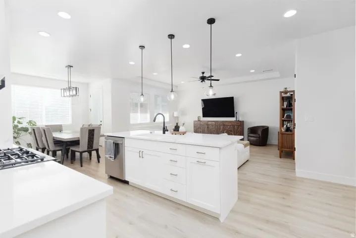Kitchen with light wood-style flooring, open floor plan, a kitchen island with sink, a ceiling fan, and light stone counters