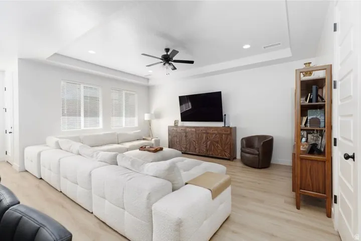 Living area featuring a raised ceiling, light wood-type flooring, ceiling fan, and recessed lighting