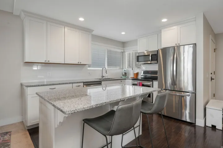 Kitchen featuring light stone counters, a breakfast bar area, stainless steel dishwasher, backsplash, and white cabinets