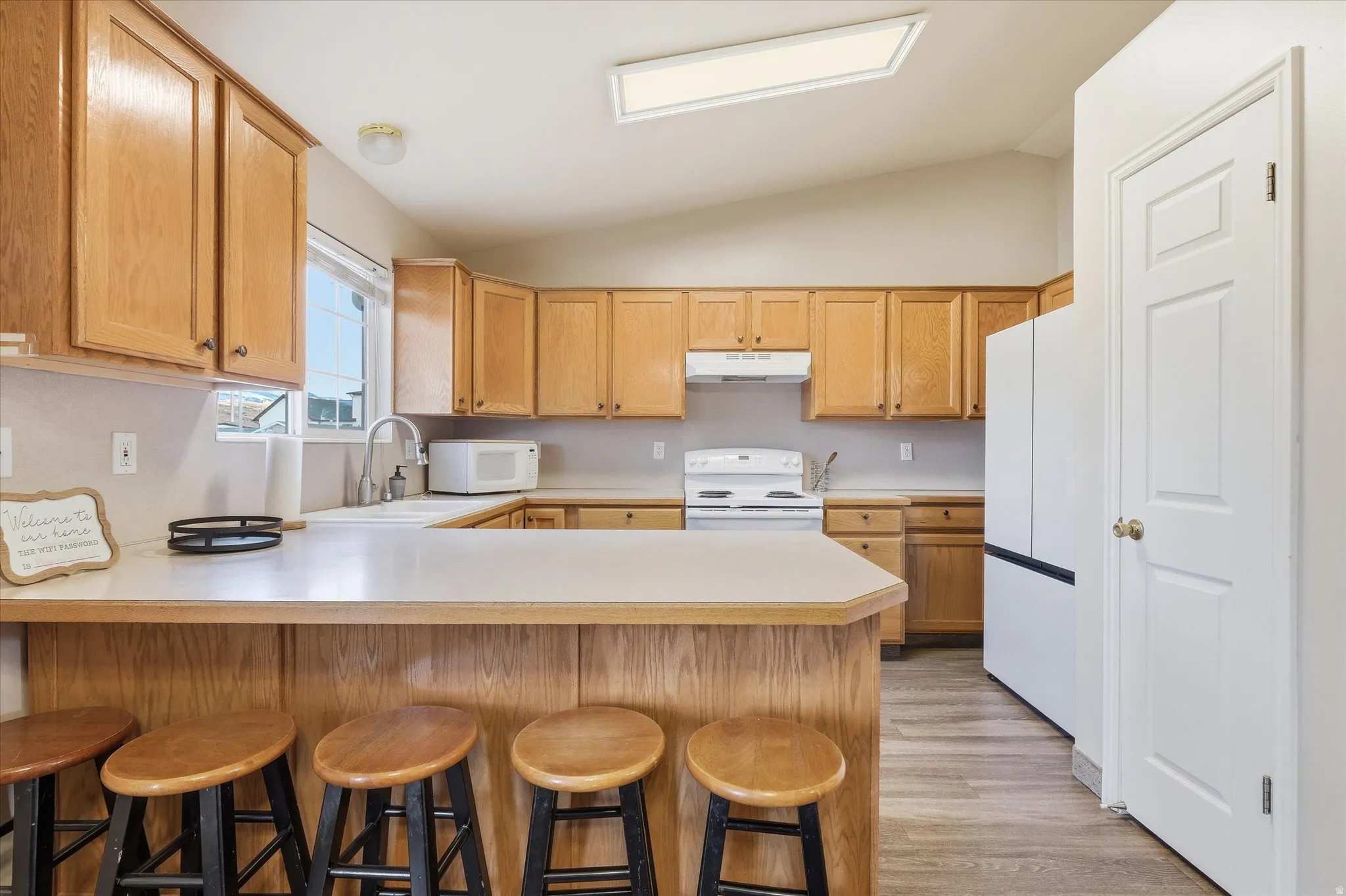 Kitchen featuring light countertops, a kitchen breakfast bar, vaulted ceiling, a peninsula, and white appliances