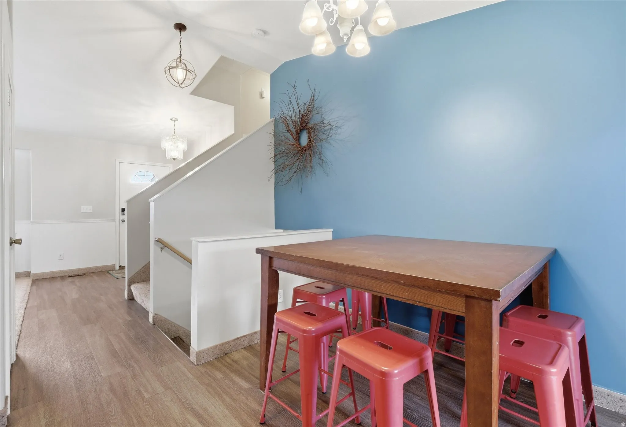 Dining room with hanging lights, light wood-type flooring, lofted ceiling, and wainscoting
