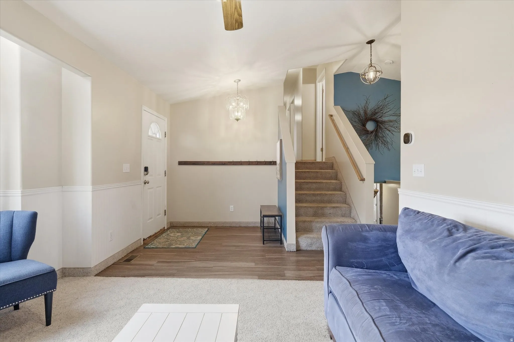 Foyer featuring a chandelier, a ceiling fan, light carpet, and wainscoting