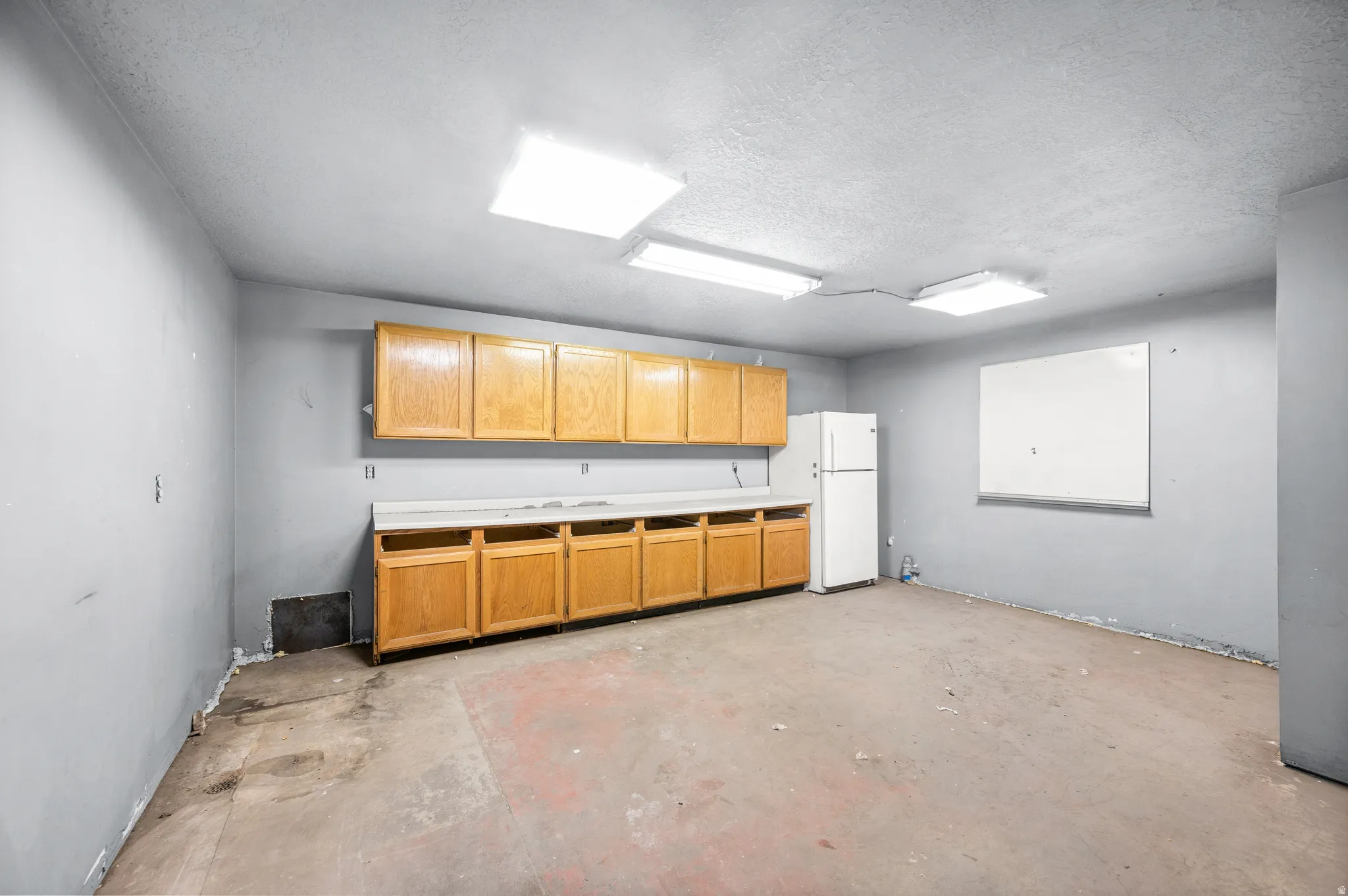 Kitchen featuring freestanding refrigerator, a textured ceiling, concrete flooring, and light countertops