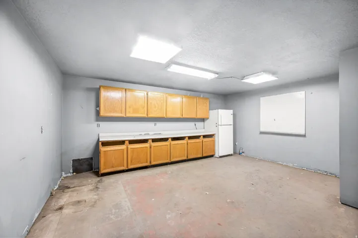 Kitchen featuring freestanding refrigerator, a textured ceiling, concrete flooring, and light countertops