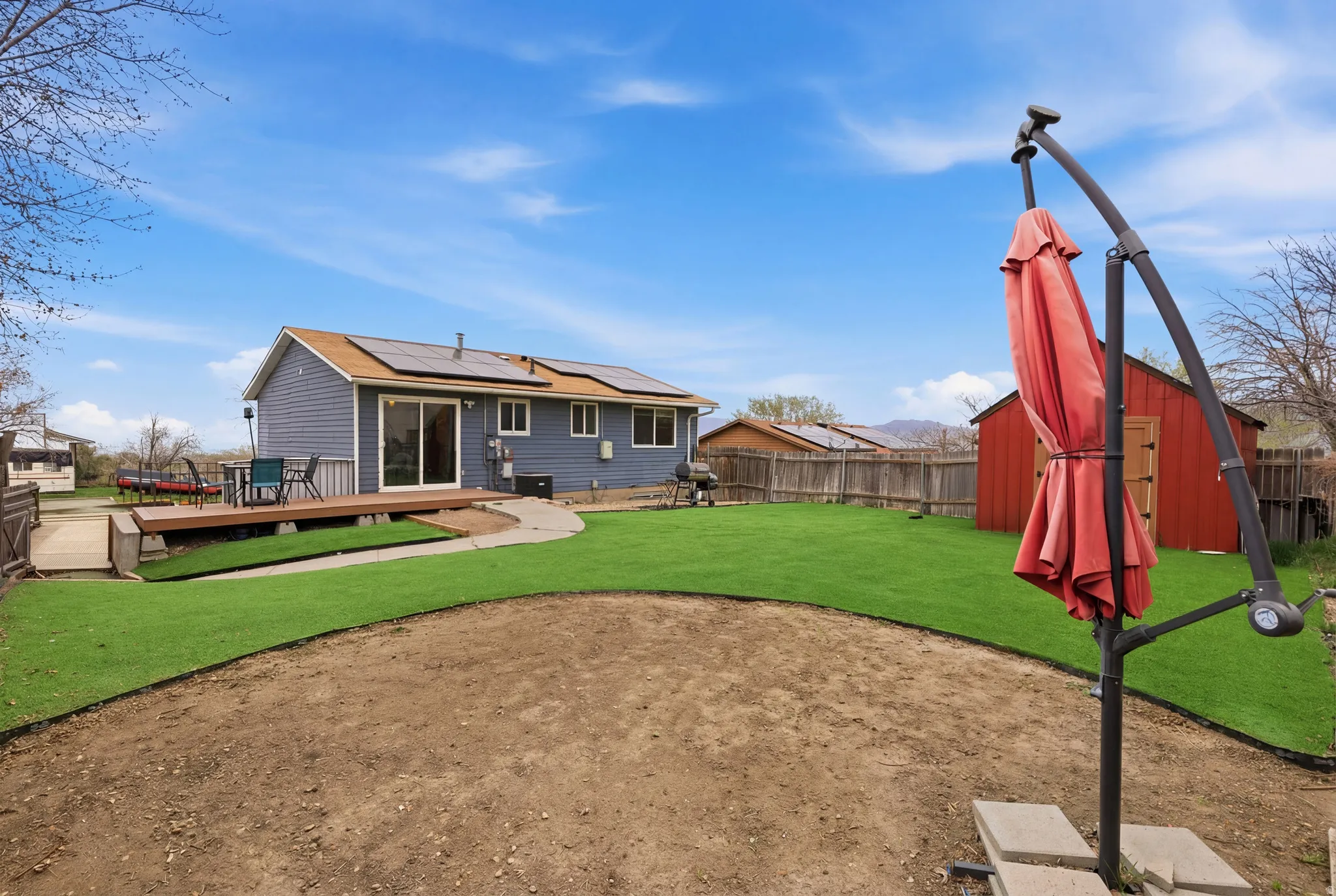 Rear view of property with roof mounted solar panels, a deck, a fenced backyard, and a storage shed