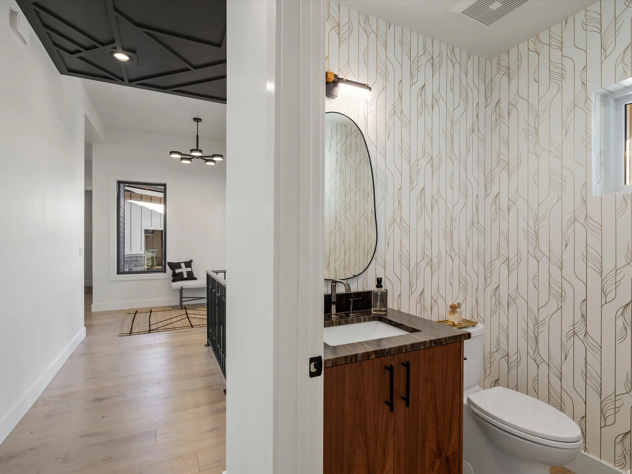 Half bathroom with vanity, light wood finished floors, and wallpapered walls